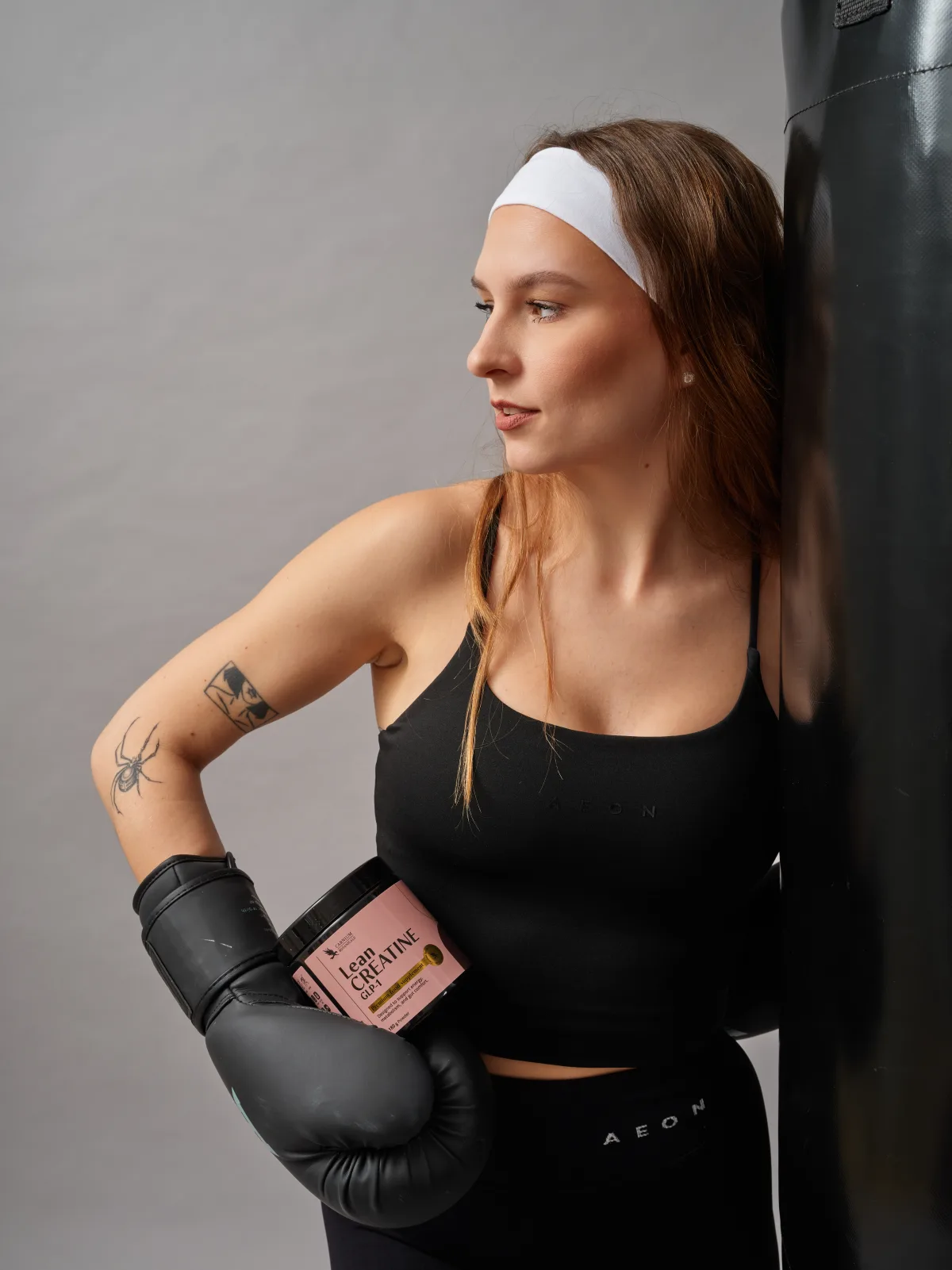 Ženska z boksarskimi rokavicami drži Lean Creatine pri vreči